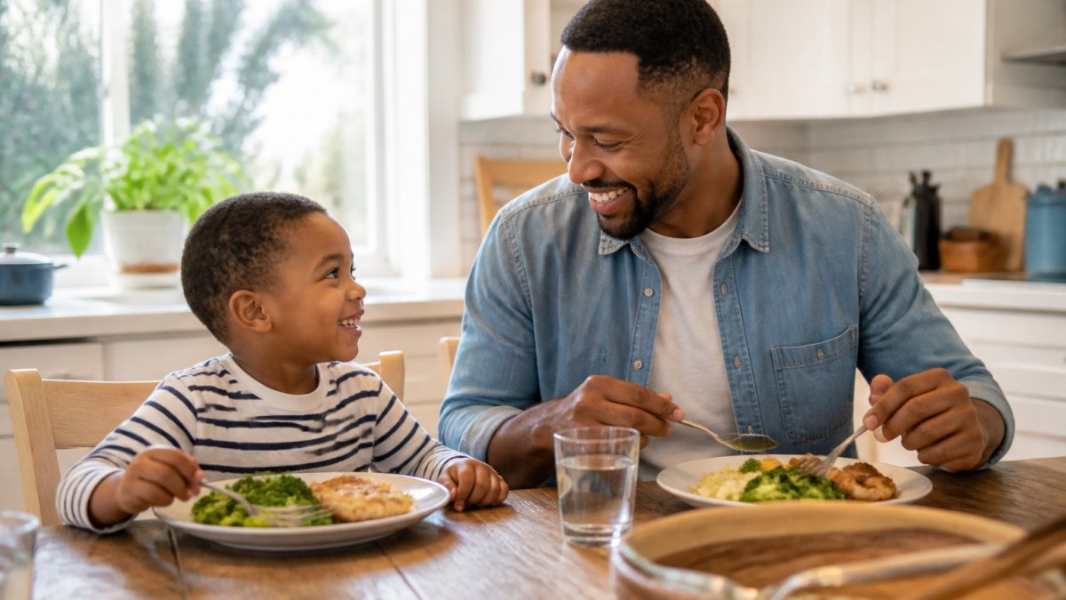 A father and young child sitting together at a kitchen table, sharing a meal and smiling, natural window lighting creating a warm family moment